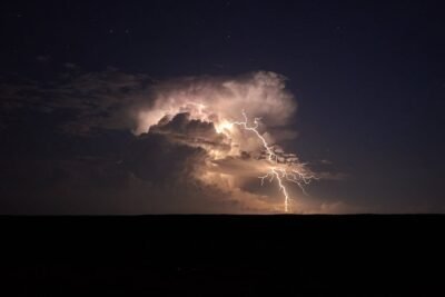 yellow lightning streaks out from a gray cloud at night over top a dark flat landscape.
