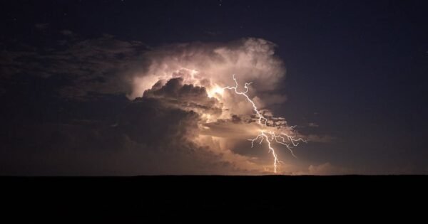 yellow lightning streaks out from a gray cloud at night over top a dark flat landscape.