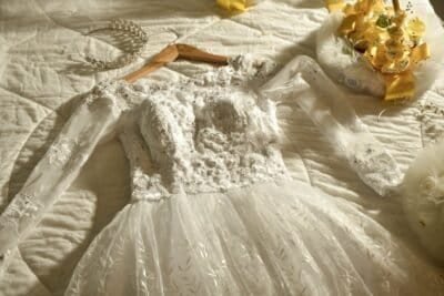 embroidered white lace wedding dress laying on a white bed next to a yellow bouquet