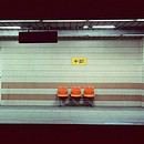 A liminal train station with three orange chairs.