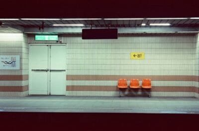 A liminal train station with three orange chairs.