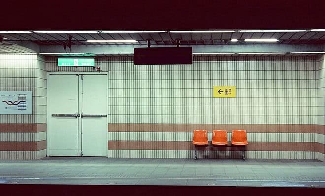 A liminal train station with three orange chairs.