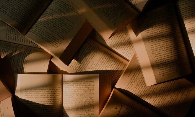 Overlapping opened books with subtle sunlight casting shadows on the pages.