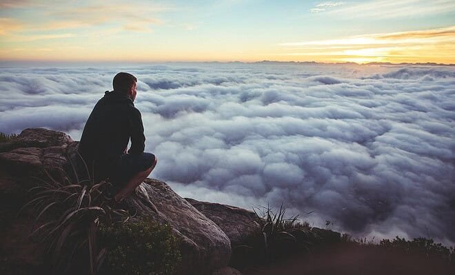 a man staring down from a mountain covered in the clouds