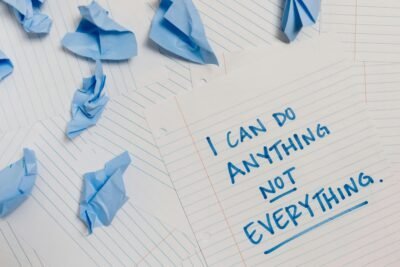 There is an array of crumpled up blue post-its and loose-leaf paper, one of the pages having the following written on it: "I can do anything, not everything."