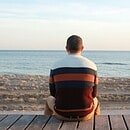 Man sitting on a wooden panel looking at the ocean