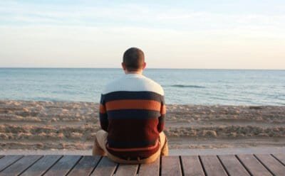 Man sitting on a wooden panel looking at the ocean