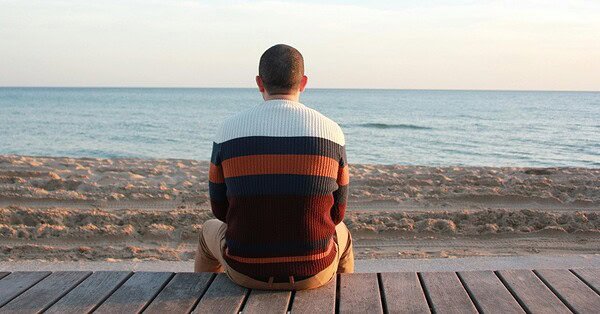Man sitting on a wooden panel looking at the ocean