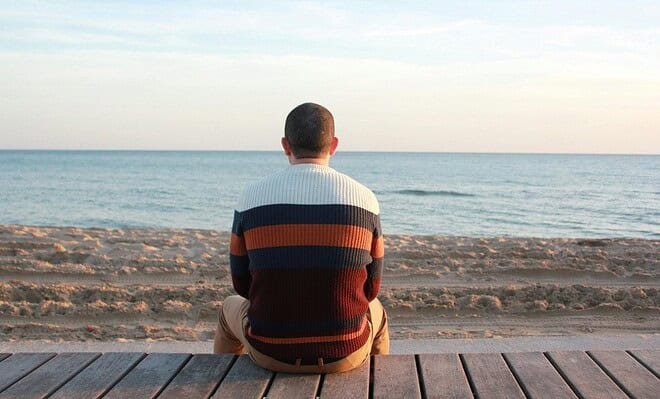 Man sitting on a wooden panel looking at the ocean