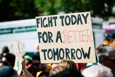 There is a protest going on with people crowded together, though the image is focused on one one specific sign being held up. The sign reads "Fight today for a better tomorrow"