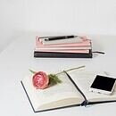 An open book on a white table with an iPhone and pink flower accents