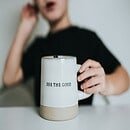 A blurred out woman in the background with a white coffee cup that reads 'see the good.