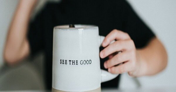 A blurred out woman in the background with a white coffee cup that reads 'see the good.