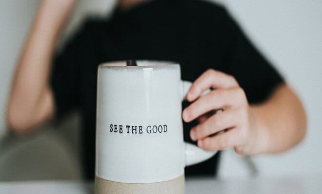 A blurred out woman in the background with a white coffee cup that reads 'see the good.