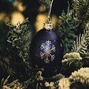 A pine tree with a blue ornament with a sparkly winter snowflake.