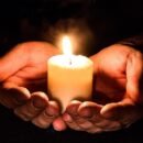 A small lit candle cupped in two hands.