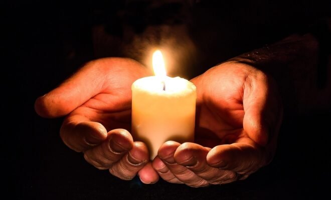 A small lit candle cupped in two hands.