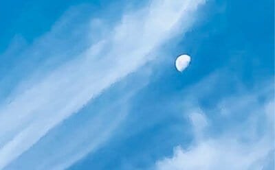 The image is of a daylight moon adrift in the wispy clouds.