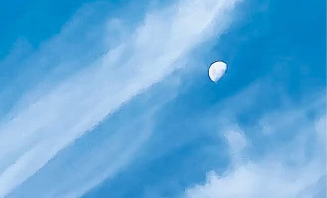 The image is of a daylight moon adrift in the wispy clouds.
