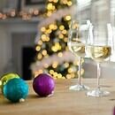 A Christmas scene with two wine glasses and various baubles on a table with a lit tree in the background