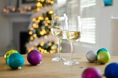 A Christmas scene with two wine glasses and various baubles on a table with a lit tree in the background