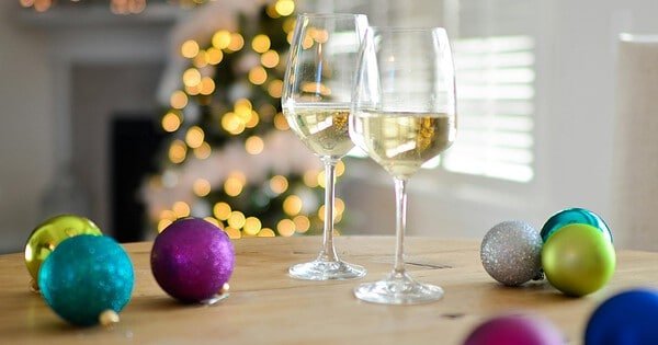 A Christmas scene with two wine glasses and various baubles on a table with a lit tree in the background