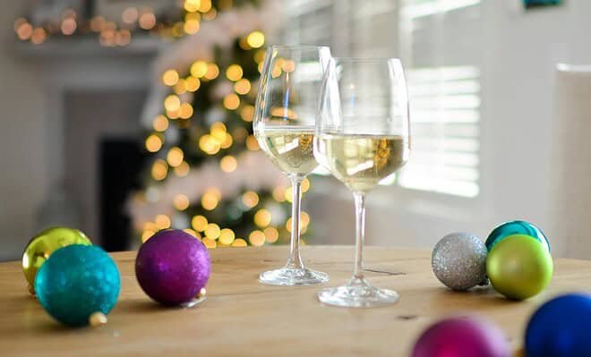 A Christmas scene with two wine glasses and various baubles on a table with a lit tree in the background