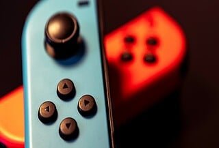 Black background with a red faded Nintento Switch controller and a blue Nintendo Switch controller in front of it.