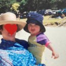 A child stares into camera, held by her mother whose anonymity is preserved through the drawing of a heart over her face.