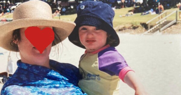 A child stares into camera, held by her mother whose anonymity is preserved through the drawing of a heart over her face.