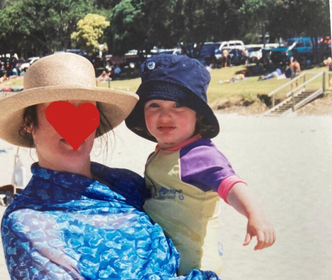 A child stares into camera, held by her mother whose anonymity is preserved through the drawing of a heart over her face.