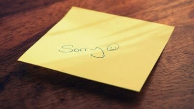 A yellow sticky note with an apology on a brown table