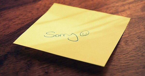 A yellow sticky note with an apology on a brown table