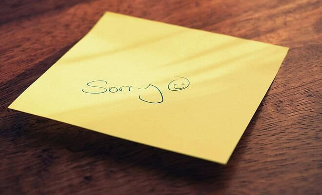 A yellow sticky note with an apology on a brown table