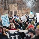 Protesters in Minneapolis gather on the spot where Renee Good was killed, holding signs that read, "When these colonies gonna rise up?", "ICE out of MN", "Renee sparkled! Fight for our neighbors". "Fuck ICE", and "ICE is not welcome (with not emphasized in red)".
