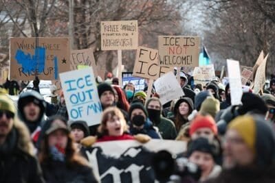 Protesters in Minneapolis gather on the spot where Renee Good was killed, holding signs that read, "When these colonies gonna rise up?", "ICE out of MN", "Renee sparkled! Fight for our neighbors". "Fuck ICE", and "ICE is not welcome (with not emphasized in red)".