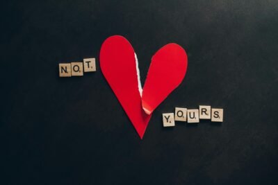 A paper made heart is shown on a black background. It is slightly torn and shows the words "not yours" on the sides of the heart, one word on either side.
