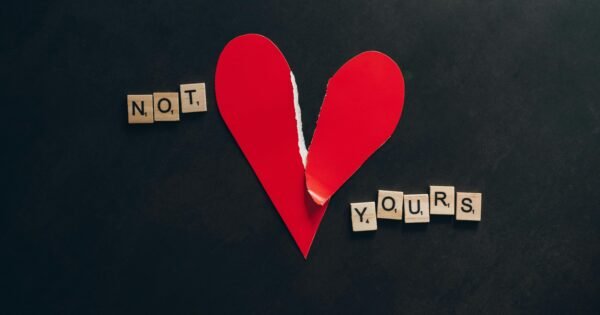 A paper made heart is shown on a black background. It is slightly torn and shows the words "not yours" on the sides of the heart, one word on either side.