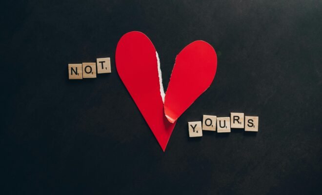A paper made heart is shown on a black background. It is slightly torn and shows the words "not yours" on the sides of the heart, one word on either side.