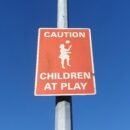 Red caution sign that says, "Caution Children at Play" under a blue sky.