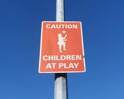 Red caution sign that says, "Caution Children at Play" under a blue sky.