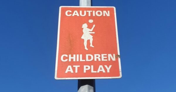 Red caution sign that says, "Caution Children at Play" under a blue sky.