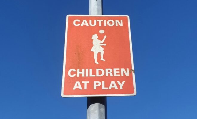 Red caution sign that says, "Caution Children at Play" under a blue sky.