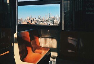A dark subway car with sun shadows shining on orange and white seats.