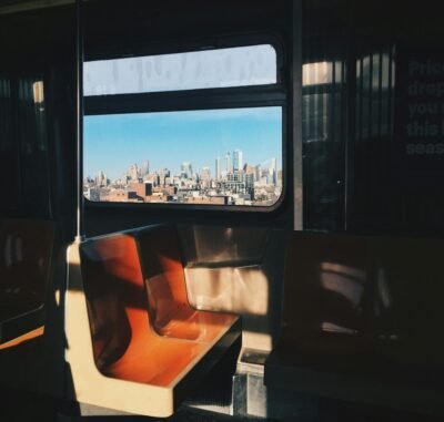 A dark subway car with sun shadows shining on orange and white seats.