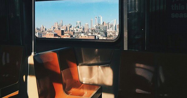A dark subway car with sun shadows shining on orange and white seats.
