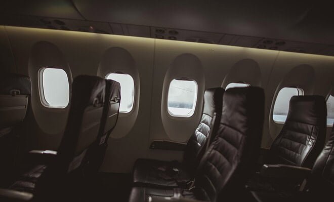 Three rows of seats line portal windows along the dimly lit interior of a commercial aircraft
