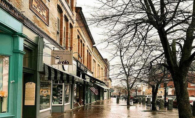 Image of small town Bath, Maine in the rain. Brick shops front a wide sidewalk lined with trees.