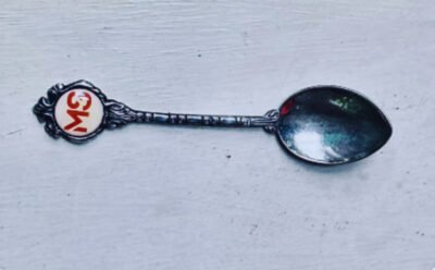 The image is of silver teaspoon with the initials "MS" (Multiple Sclerosis) embossed on the handle button.