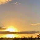 The image is of the sun setting behind a ribbon of clouds